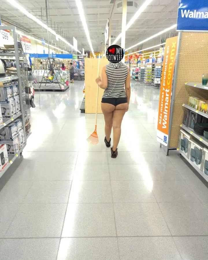 Femme vue de dos, portant un haut rayé et un short noir, tenant une balayette, dans un magasin Walmart.
