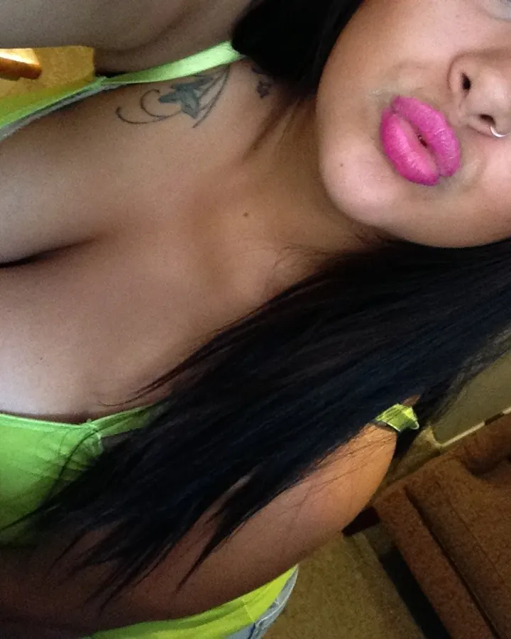 Femme aux cheveux noirs portant un haut vert, faisant un baiser à l'appareil photo.