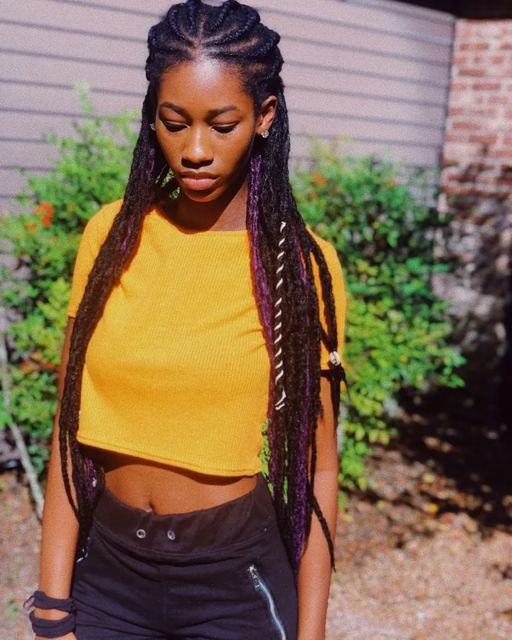 Femme africaine aux cheveux noirs, portant un crop-top jaune et un pantalon noir, avec des tresses colorées.